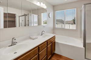 Bathroom in Primary bedroom  featuring a shower stall, a garden tub, double vanity, walk in closet and wood finished floors.