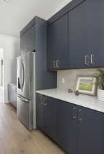 Kitchen featuring blue cabinetry, light wood-style flooring, stainless steel refrigerator with ice dispenser, and light countertops