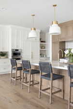 Kitchen with light wood-style flooring, light countertops, a kitchen bar, open shelves, and decorative light fixtures