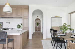Kitchen with arched walkways, wood finished floors, light countertops, a breakfast bar, and recessed lighting