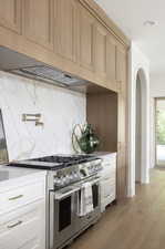 Kitchen featuring stainless steel range, light wood-type flooring, decorative backsplash, recessed lighting, and arched walkways