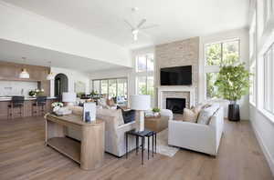 Living area with light wood-type flooring, arched walkways, a towering ceiling, a ceiling fan, and a fireplace