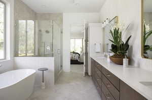 Bathroom featuring a shower stall, double vanity, a soaking tub, wallpapered walls, and ensuite bath