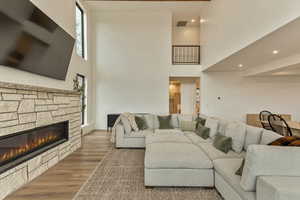 Living room featuring a high ceiling, a fireplace, wood finished floors, plenty of natural light, and recessed lighting