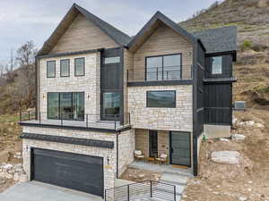 Contemporary house featuring a balcony, an attached garage, stone siding, and driveway