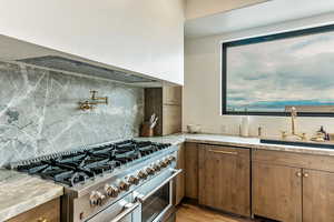 Kitchen featuring double oven range, tasteful backsplash, premium range hood, light wood-style floors, and brown cabinetry