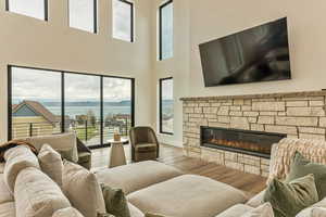 Living area with wood finished floors, plenty of natural light, a stone fireplace, and a high ceiling