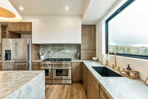 Kitchen featuring high quality appliances, brown cabinets, light wood-style flooring, tasteful backsplash, and light stone counters