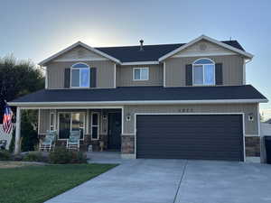 Craftsman house featuring a porch, stone siding, an attached garage, driveway, and a front lawn