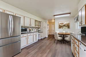 Kitchen featuring stainless steel appliances, dark countertops, dark wood-style flooring, decorative backsplash, and glass insert cabinets