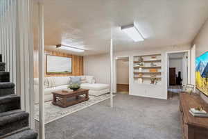 Carpeted living area with a textured ceiling, stairs, built in features, and wooden walls