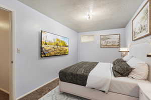 Carpeted bedroom featuring a textured ceiling and baseboards