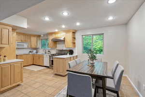 Kitchen with light countertops, recessed lighting, light brown cabinets, white appliances, and under cabinet range hood