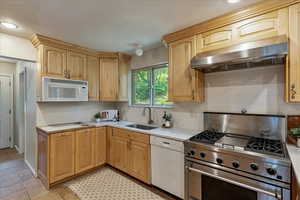 Kitchen featuring white appliances, under cabinet range hood, light countertops, tasteful backsplash, and light brown cabinetry