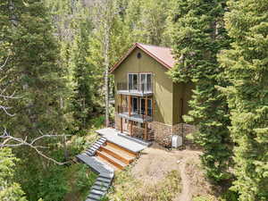 Front  view of property with a balcony, stone siding, a forest view, a metal roof, and a porch