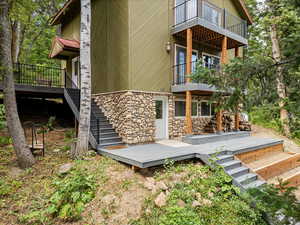 Rear view of house with a balcony, stairs, stone siding, and a deck