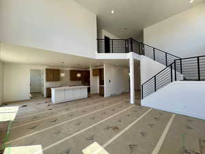 Unfurnished living room featuring a high ceiling, stairs, and recessed lighting