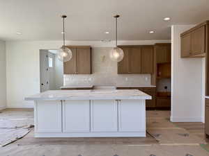 Kitchen with decorative backsplash, light countertops, brown cabinets, a center island, and recessed lighting