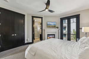 Bedroom with a glass covered fireplace, light colored carpet, a ceiling fan, and connected bathroom