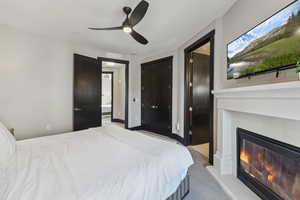 Bedroom with light colored carpet, a glass covered fireplace, and ceiling fan