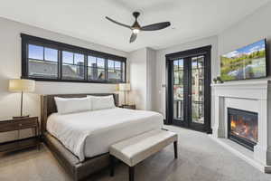 Carpeted bedroom with access to exterior, multiple windows, a glass covered fireplace, and a ceiling fan