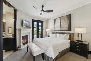 Bedroom with a glass covered fireplace, ceiling fan, access to exterior, and light colored carpet