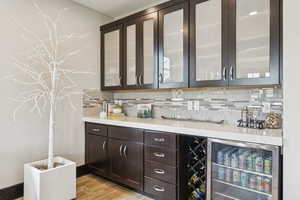 Indoor bar featuring wine cooler, decorative backsplash, and light wood-style flooring