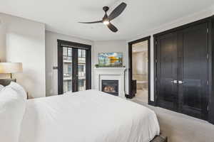 Carpeted bedroom featuring ensuite bathroom, a glass covered fireplace, and ceiling fan