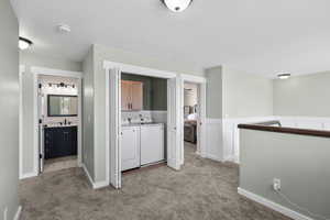 Hallway featuring independent washer and dryer, light colored carpet, a textured ceiling, and a wainscoted wall
