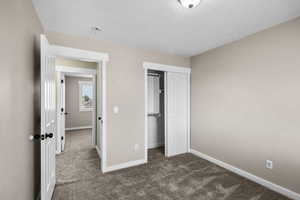 Unfurnished bedroom featuring dark carpet, a textured ceiling, and a closet