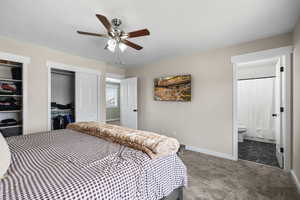 Carpeted bedroom with multiple closets, ensuite bath, and a ceiling fan