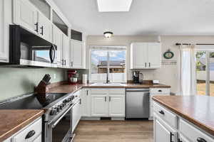 Kitchen with appliances with stainless steel finishes, dark countertops, white cabinetry, light wood-style flooring, and a textured ceiling