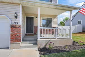 Property entrance featuring covered porch, brick siding, and a garage
