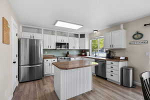 Kitchen with appliances with stainless steel finishes, white cabinets, light wood-style floors, a center island, and a textured ceiling