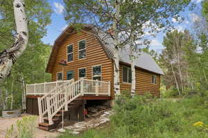 Back of house featuring a wooden deck, a gambrel roof, a metal roof, stairway, and log veneer siding