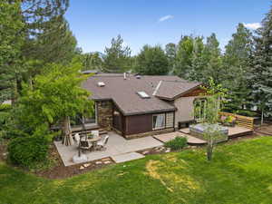 Rear view of property featuring a shingled roof, a yard, a wooden deck, and a patio