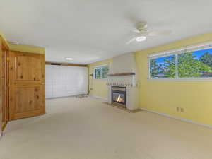 Unfurnished living room with a fireplace, carpet flooring, and ceiling fan