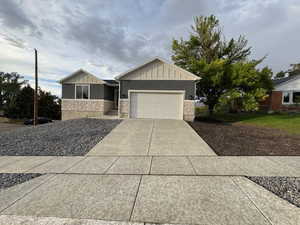 View of front facade featuring board and batten siding, driveway, an attached garage, and stone siding