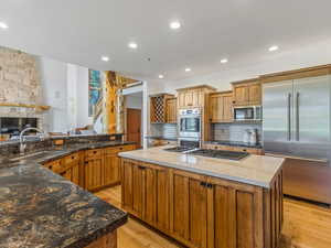 Kitchen with a large island, stainless steel appliances, decorative backsplash, brown cabinetry, and recessed lighting