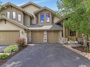 View of front of home with stone siding, a garage, driveway, stucco siding, and roof with shingles