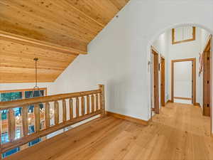 Hallway with arched walkways, light wood finished floors, a wood ceiling with exposed beams, and high vaulted ceiling