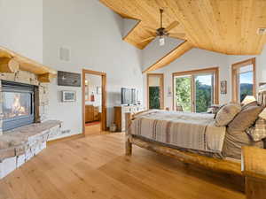 Bedroom with wood ceiling, vaulted ceiling, light wood-style flooring, a stone fireplace, and connected bathroom
