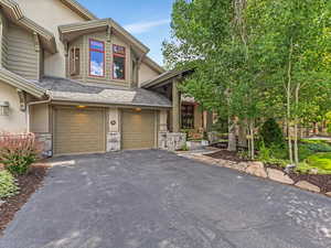 View of front facade featuring asphalt driveway, an attached garage, stone siding, and stucco siding