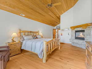 Bedroom with wood ceiling, a fireplace, light wood-style floors, high vaulted ceiling, and a ceiling fan