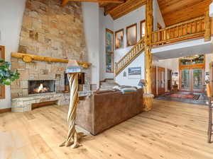 Living area featuring a wood ceiling with exposed beams, a stone fireplace, wood finished floors, high vaulted ceiling, and stairway