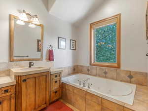 Full bath featuring vanity, vaulted ceiling, and a jetted tub