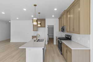 Kitchen featuring appliances with stainless steel finishes, tasteful backsplash, light wood-style flooring, pendant lighting, and light countertops