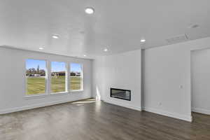 Unfurnished living room with dark wood-type flooring, recessed lighting, and a glass covered fireplace