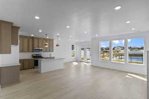 Kitchen featuring open floor plan, appliances with stainless steel finishes, a center island with sink, brown cabinetry, and light wood-type flooring