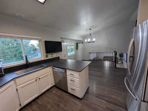 Kitchen with new Dekton dark countertops, stainless steel appliances, dark wood-style flooring, a peninsula, and a chandelier